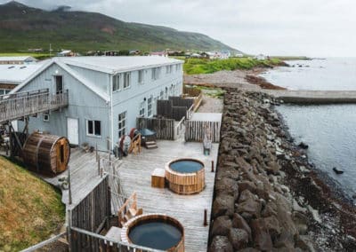 Aerial shot of the house beloning to Blabjorg guesthouse, with patio and hot pots, agains the rocky coastline