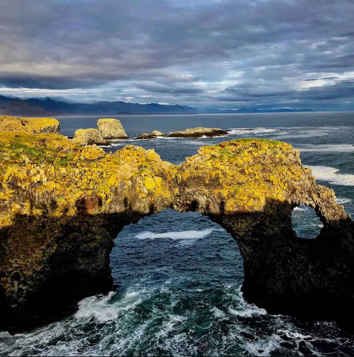 A sea rock with an arch at dusk with shadows of people