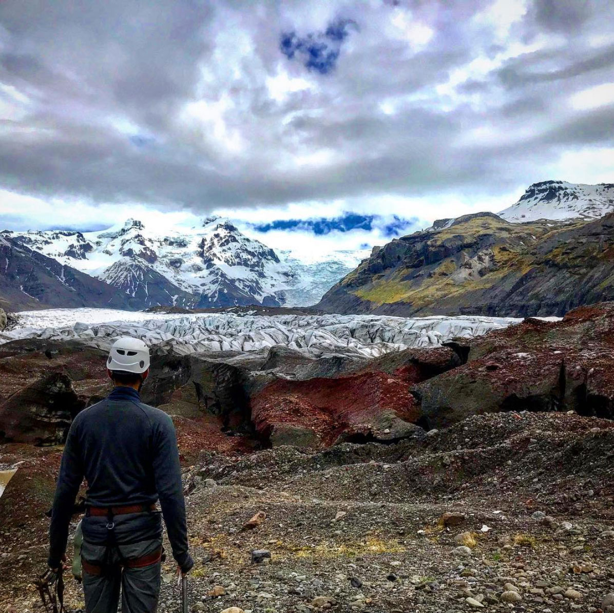 A solitary person fronting a glacier and red lava rock