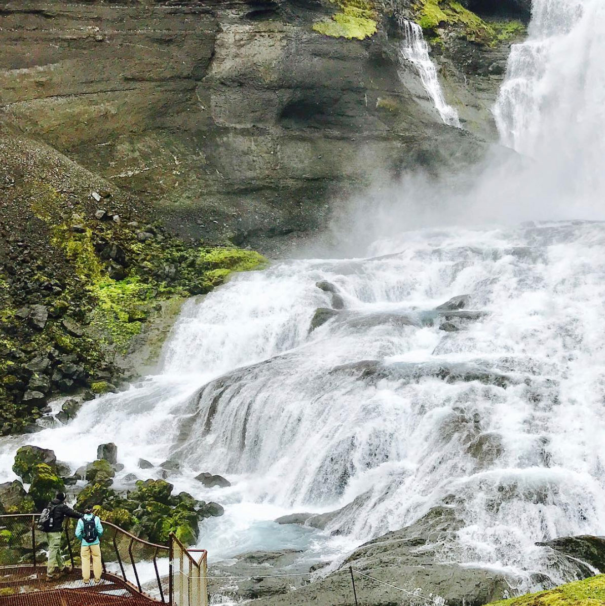 Two persons standing on a balcony looking towards cascading water