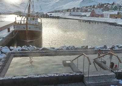 winter scene from Siglufjordur village and harbour with a boat and few people sitting in a hot tub