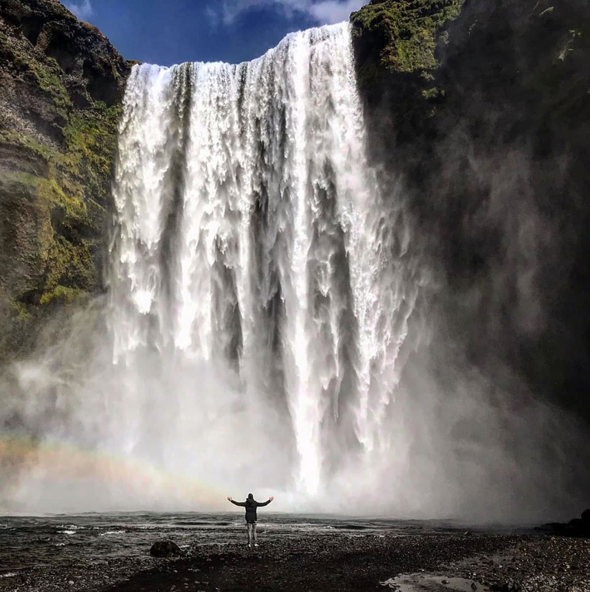 Person standing alone and facing the Skogafoss waterfall