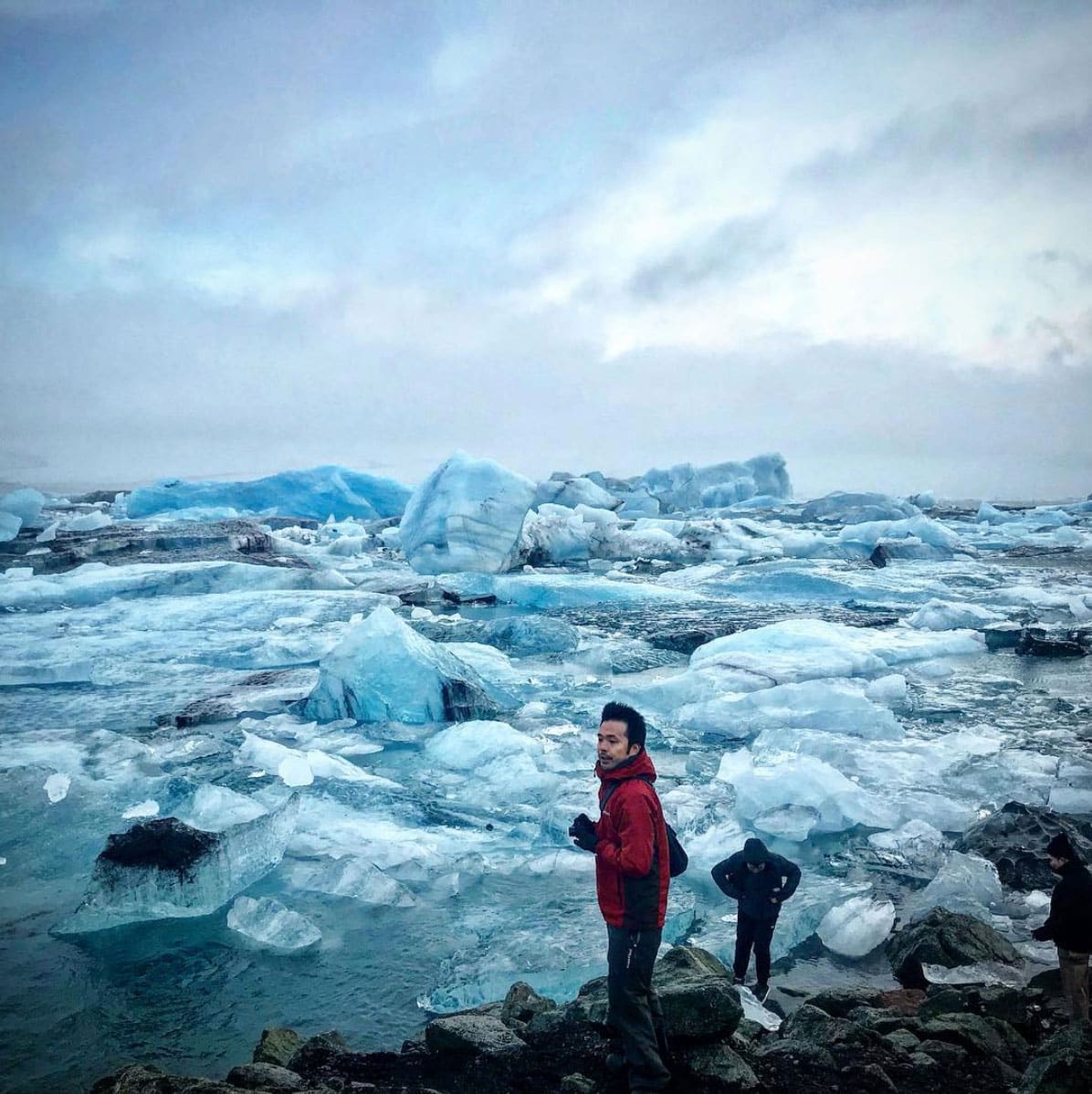 Two men standing on the shore of the Glacier Lagoon with icebergs in background