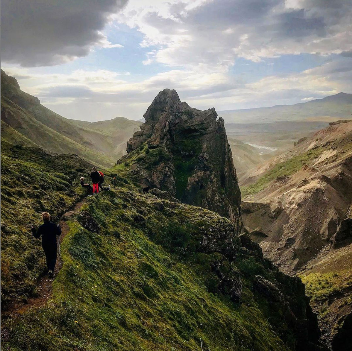 Hikers walking on a green hill-side with a peak and distant horizon in the background