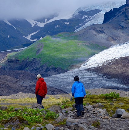 Two persons walking on a hill with the glacier in the background