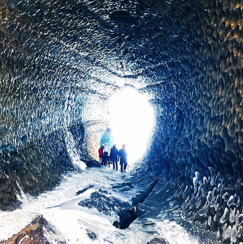 A group of hikers walking through an ice tunnel towards light